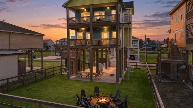 Ein mehrstöckiges Haus mit Terrasse, Feuerstelle und Blick auf den Sonnenuntergang.