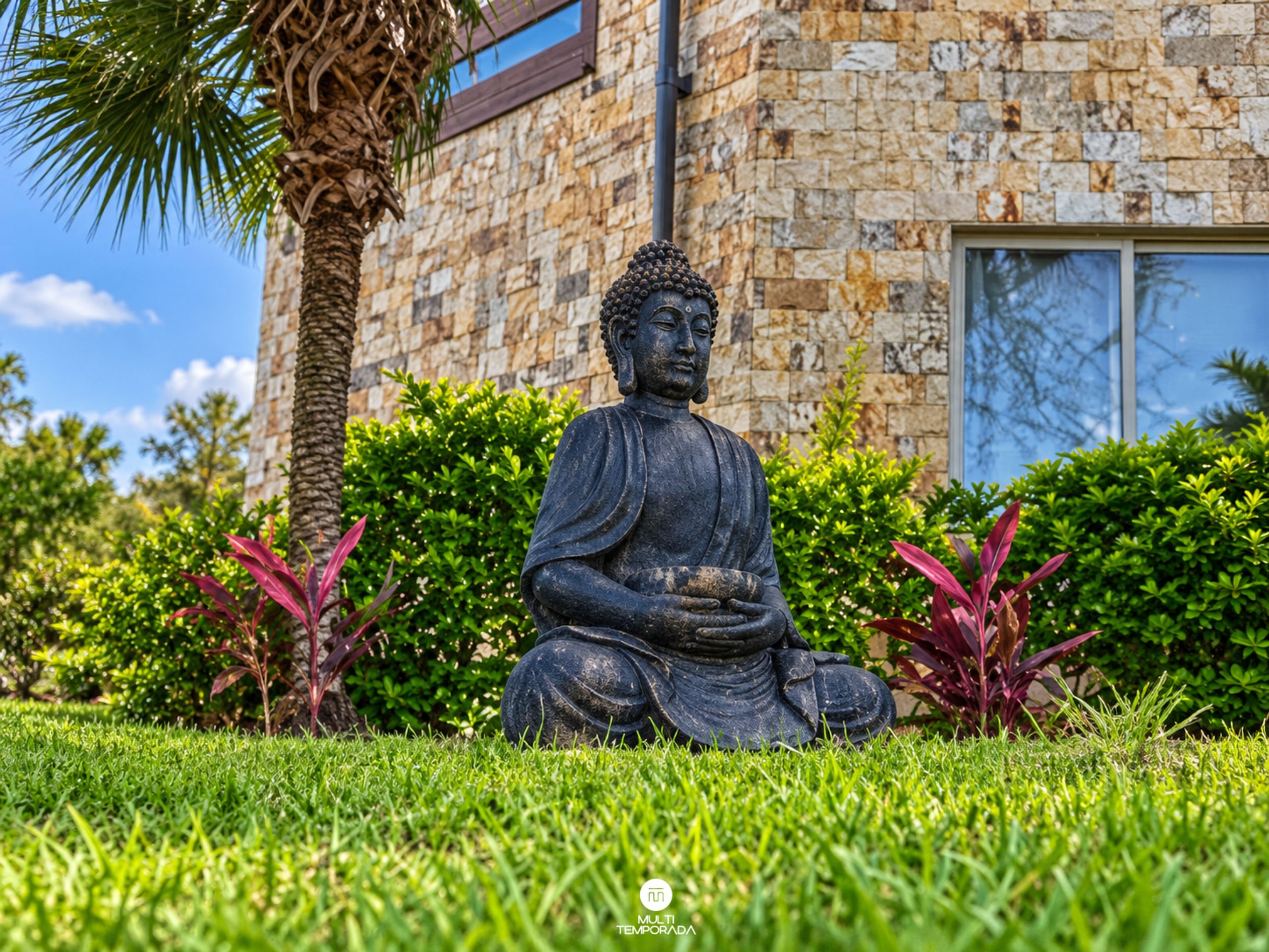 Una estatua de Buda en un jardín con un edificio de piedra al fondo.
