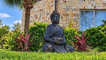 Una estatua de Buda en un jardín con un edificio de piedra al fondo.