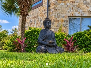 Uma estátua de Buda em um jardim com um edifício de pedra ao fundo.