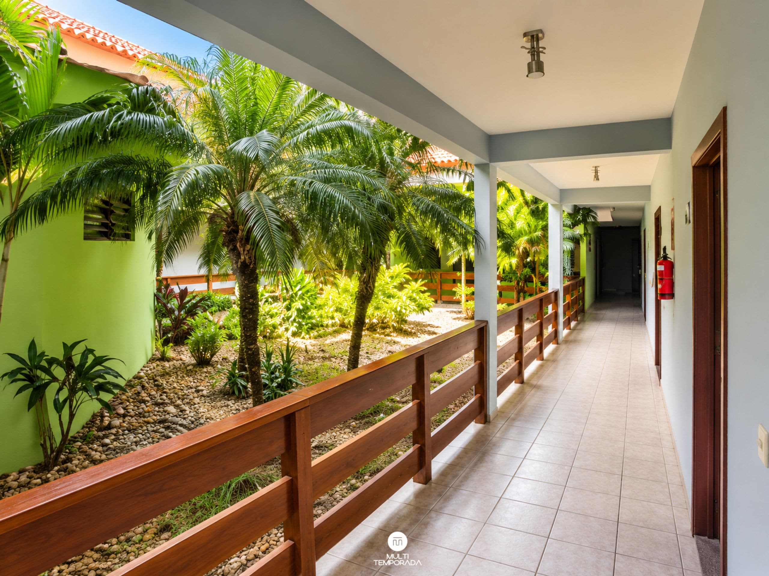 A corridor with a wooden railing, green walls, and palm trees.