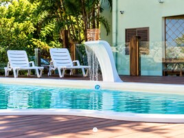 Piscina com duas espreguiçadeiras brancas e um recurso aquático.