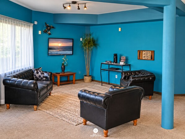 A living room with blue walls, two leather sofas, a coffee table, a TV, and a plant.