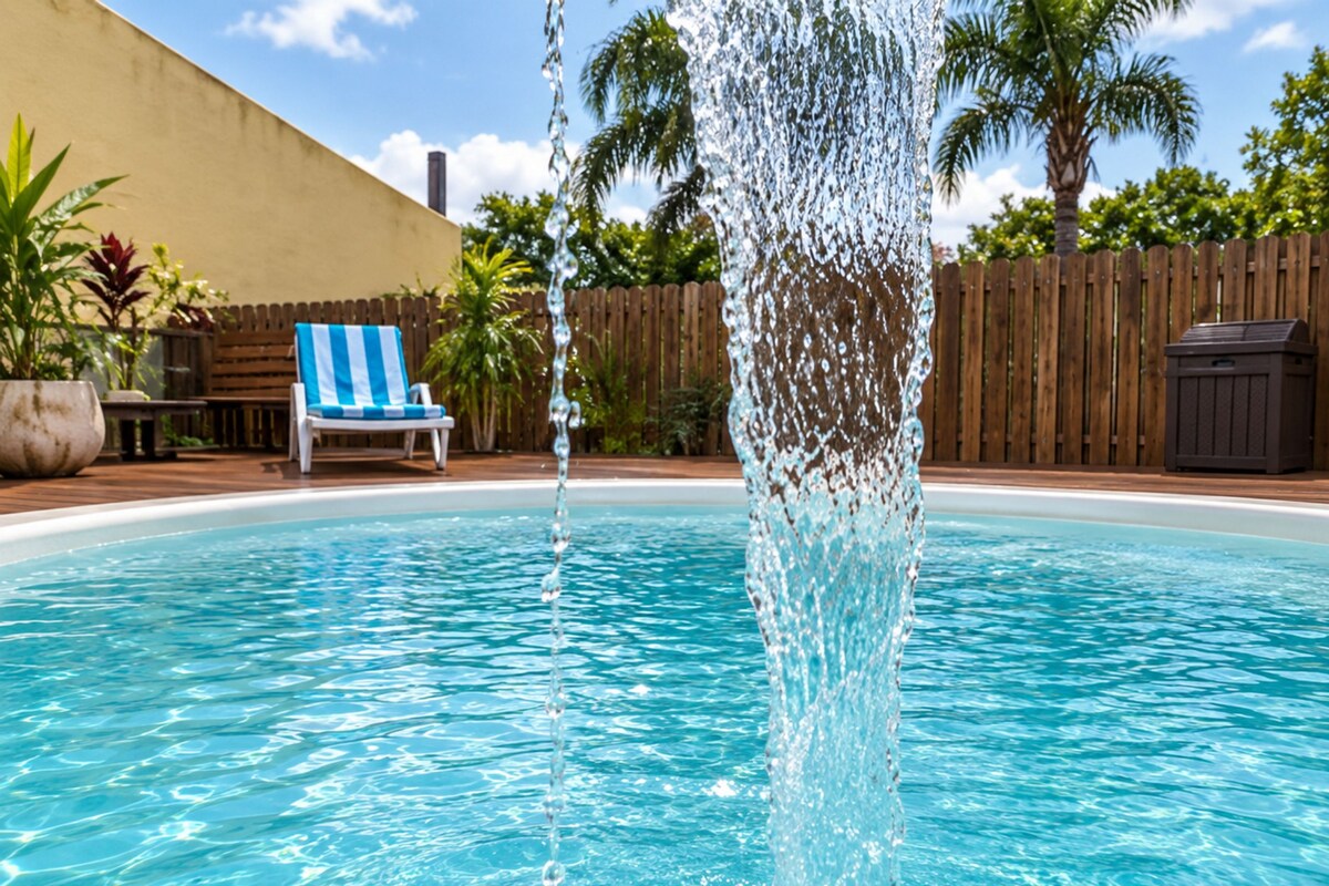 Piscina com água azul cristalina, cerca de madeira e espreguiçadeira listrada em azul e branco.