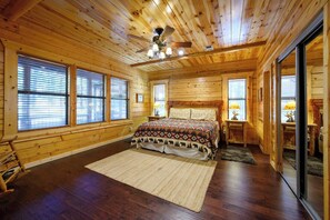 A log cabin bedroom with a bed, a ceiling fan, and large windows. - Castaway Lodge - spacious cabin with private rooms (Broken Bow)