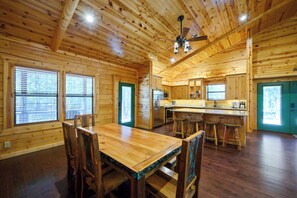 A wooden interior with a dining table, chairs, a kitchen area, and a ceiling fan. - Castaway Lodge - spacious cabin with private rooms (Broken Bow)
