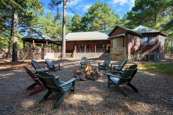 A lodge with a fire pit surrounded by Adirondack chairs, a stone fireplace, and a covered deck. - Castaway Lodge - spacious cabin with private rooms (Broken Bow)