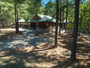 A rustic cabin with a stone foundation, surrounded by tall pine trees. - Castaway Lodge - spacious cabin with private rooms (Broken Bow)