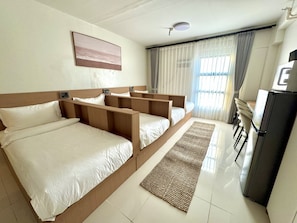 Una camera d'albergo con un letto grande, una scrivania, un frigorifero e una finestra con tende.
