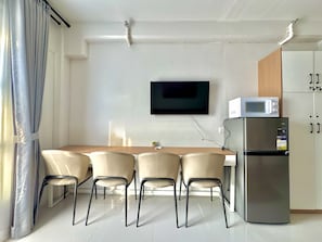 A modern kitchen with a flat-screen TV, a microwave, and a refrigerator. There are four chairs around a wooden table. - Royal Oceancrest Panglao 1 (Dauis)