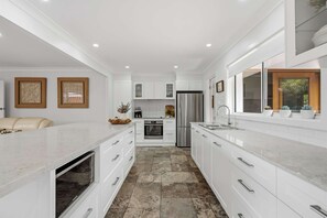A modern kitchen with white cabinetry, a stainless steel refrigerator, and a large island with a built-in oven. - Aura by Coast Hosting (Terrigal)