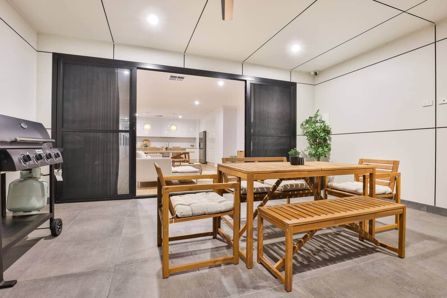 A modern kitchen with a dining area, featuring a grill, wooden furniture, and a view into the living space.