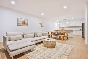 En moderne stue med sofa, spisebord og et køkken i baggrunden.