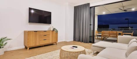 A modern living room with a flat-screen TV, a wooden cabinet, a round wicker coffee table, and a sofa.
