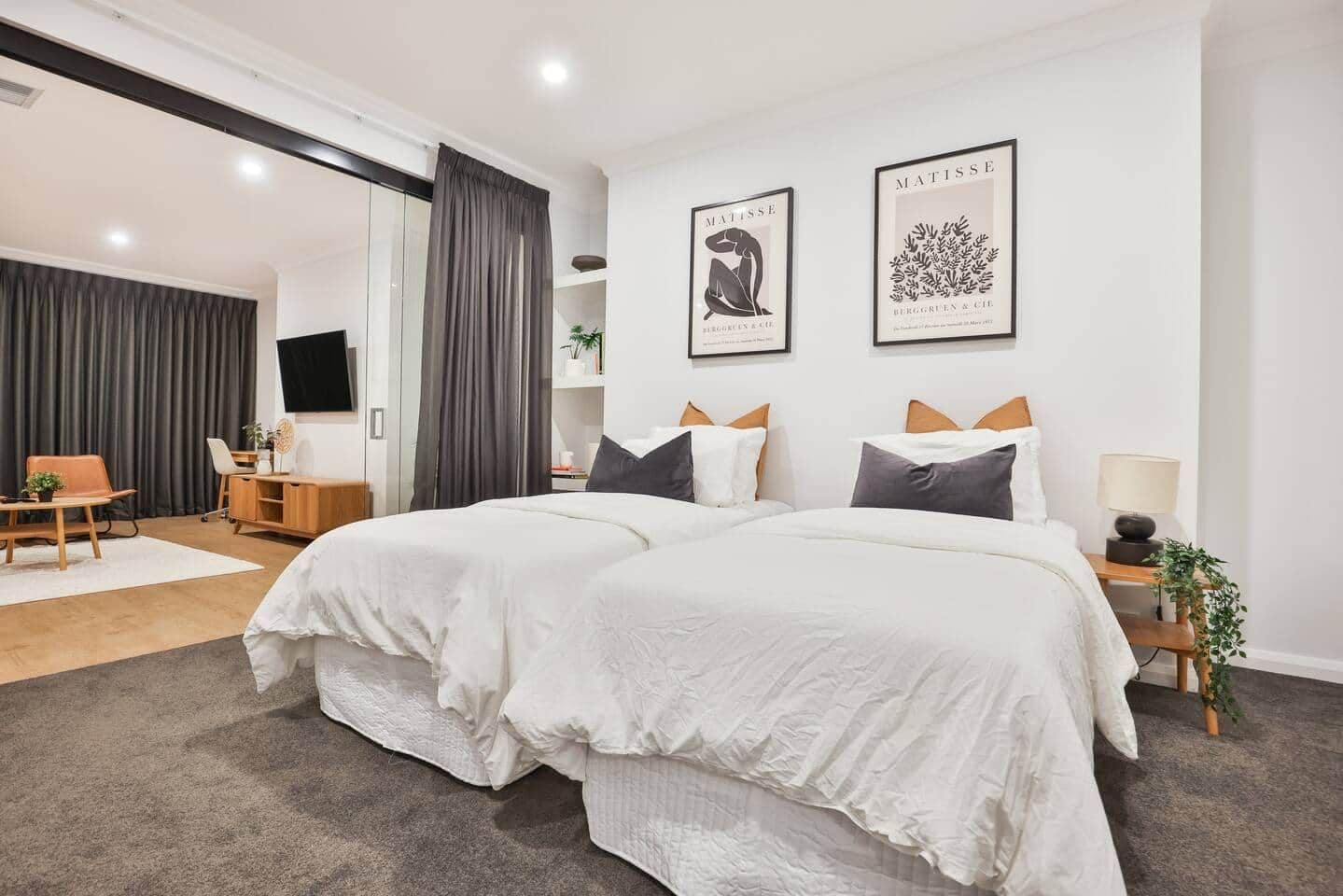 A modern bedroom with a large bed, two framed artworks, a desk, and a chair.
