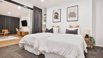A modern bedroom with a large bed, two framed artworks, a desk, and a chair.