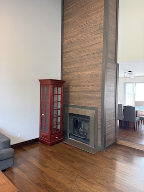 A room with a fireplace, wooden flooring, and a tall, narrow cabinet. - Beautifull Luxury House by Canion Meadows Golf Course (Calgary)