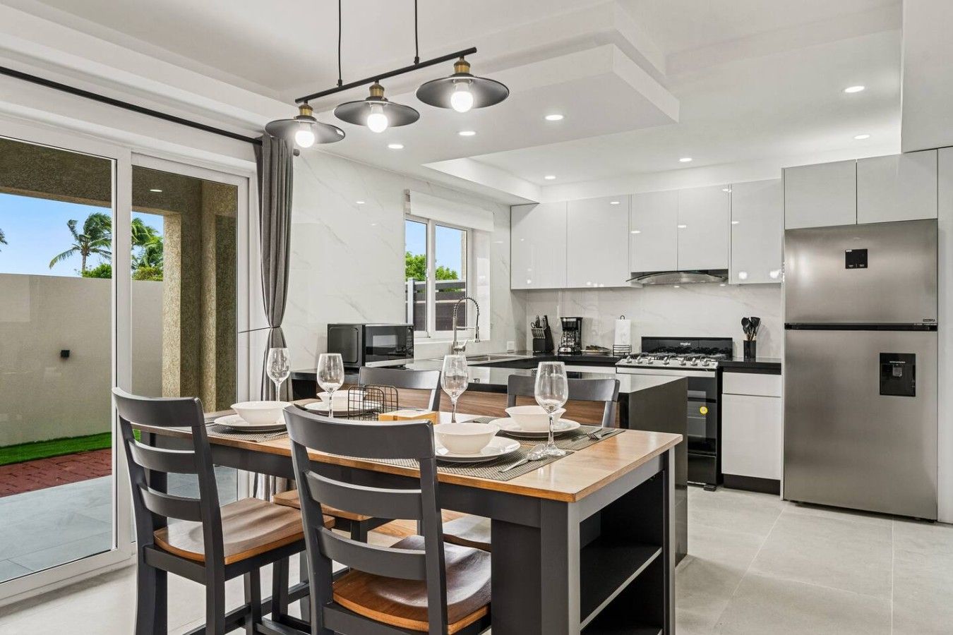 A modern kitchen with stainless steel appliances, a dining area with a table set for four, and a view of the outdoors.
