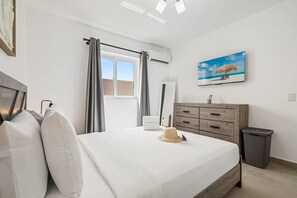 Ein Hotelzimmer mit Bett, Schminktisch, Spiegel, Fernseher und einem Fenster mit Vorhängen.