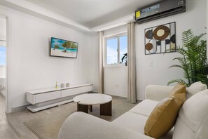 Un salon moderne avec un canapé blanc, une table basse ronde, une console blanche, un tableau et une grande fenêtre avec des rideaux.