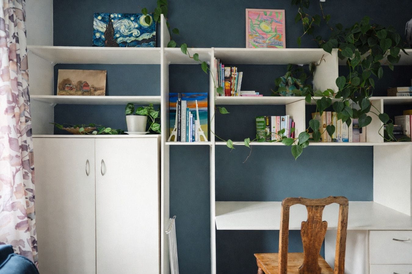 Une pièce avec un meuble blanc, une chaise en bois et une bibliothèque contenant des livres et des plantes.