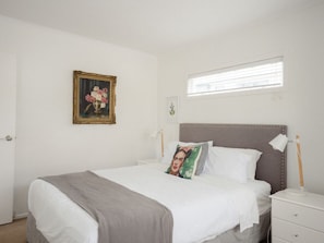 A bedroom with a bed, a nightstand, a lamp, a window, and a framed picture on the wall. - Marigold by Homello (Auckland)