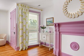 A room with a pink door, a white and yellow patterned curtain, a white dresser with a vase of flowers, and a pink fireplace. - Everett Estate | Modern Luxury Meets Historic Charm (Nellysford)