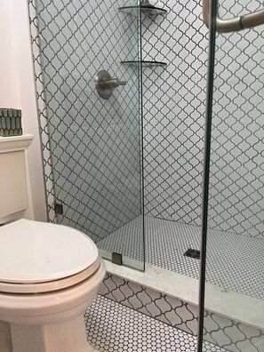 A bathroom with a toilet, a shower with a glass door, and a patterned floor.