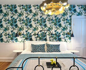 A bedroom with a bed, two bedside tables, a chandelier, and a floral wallpaper.