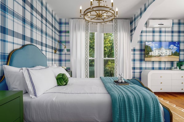 A bedroom with a bed, a nightstand, a dresser, a chandelier, and a window with curtains.
