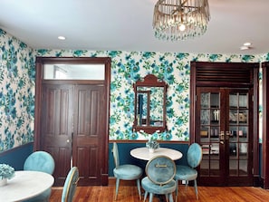 A room with a wooden door, a round table with chairs, a mirror, and a chandelier.