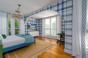 A bedroom with a bed, a desk, and a chair. There is a window with curtains and a view of trees.