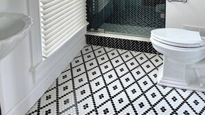 A bathroom with a white toilet, a glass-enclosed shower, and a patterned floor. - Everett Estate | King Suite + Twin Daybed (Nellysford)