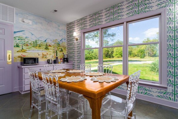A dining area with a wooden table, clear chairs, and a view of a green landscape through large windows.