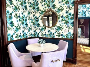 Ein Zimmer mit floralem Wandpapier, einem runden Tisch mit Stühlen und einem Spiegel an der Wand.