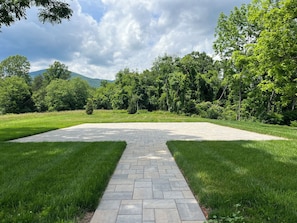 A paved pathway leading to a grassy area with trees and a mountain in the background.