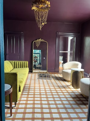 A room with a green sofa, a checkered floor, a mirror with a gold frame, and a unique chandelier.