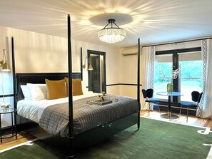 A four-poster bed with a modern design, a chandelier, and a view of the outdoors through a large window.
