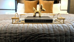 A neatly made bed with a quilted cover, a tray with a book titled 'GUCCI THE MAKING OF', and a decorative golden horse figurine on the bed. - Everett Estate | King Suite + Twin Daybed (Nellysford)