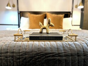 Ein ordentlich bezogenes Bett mit einer gesteppten Decke, ein Tablett mit einem Buch mit dem Titel 'GUCCI THE MAKING OF' und eine dekorative goldene Pferdefigur auf dem Bett.