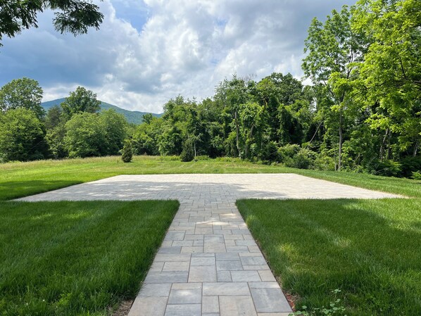 A paved pathway leading to a grassy area with trees and a mountain in the background.