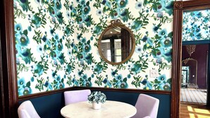 A room with a floral wallpaper, a round table with chairs, and a mirror on the wall. - Everett Estate | Queen Suite + Covered Porch (Nellysford)