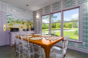 A dining area with a wooden table, clear chairs, and a view of a green landscape through large windows. - Everett Estate | Mountain View King Suite (Nellysford)