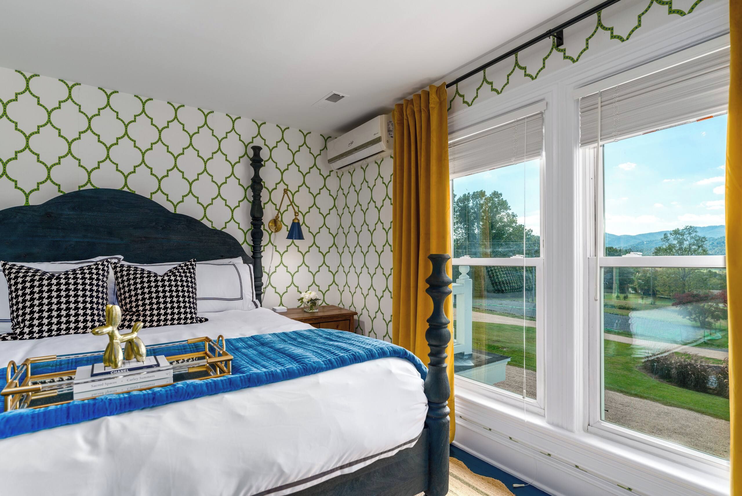 A bedroom with a bed, a nightstand, a lamp, and a window with a view of the outdoors.