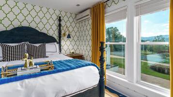 A bedroom with a bed, a nightstand, a lamp, and a window with a view of the outdoors.