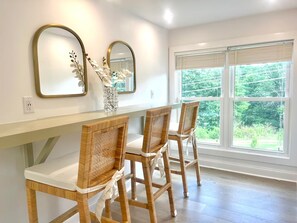A dining area with a white table, two wicker chairs, and a vase with white flowers. - Everett Estate | Private Loft + Mountain Views (Nellysford)