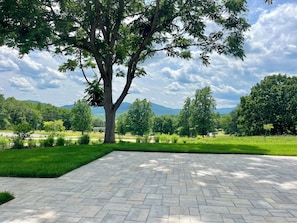 A paved outdoor area with a large tree and a view of a green landscape. - Everett Estate | Private Loft + Mountain Views (Nellysford)