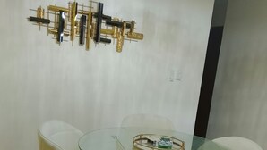 Un comedor con mesa de vidrio rodeada de sillas blancas con patas doradas.