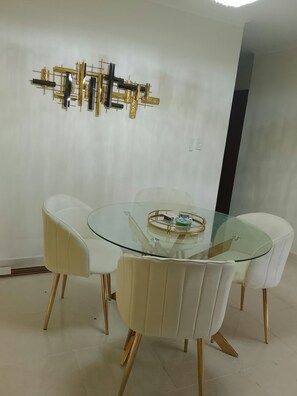 Zona pranzo con tavolo in vetro circondato da sedie bianche a gambe dorate.