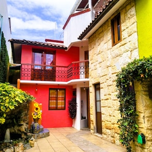 A two-story building with a red facade and a stone wall. - Guelaguetza Terrace House, Oaxaca—10 minutes from downtown, ideal for families. (Oaxaca de Juárez)